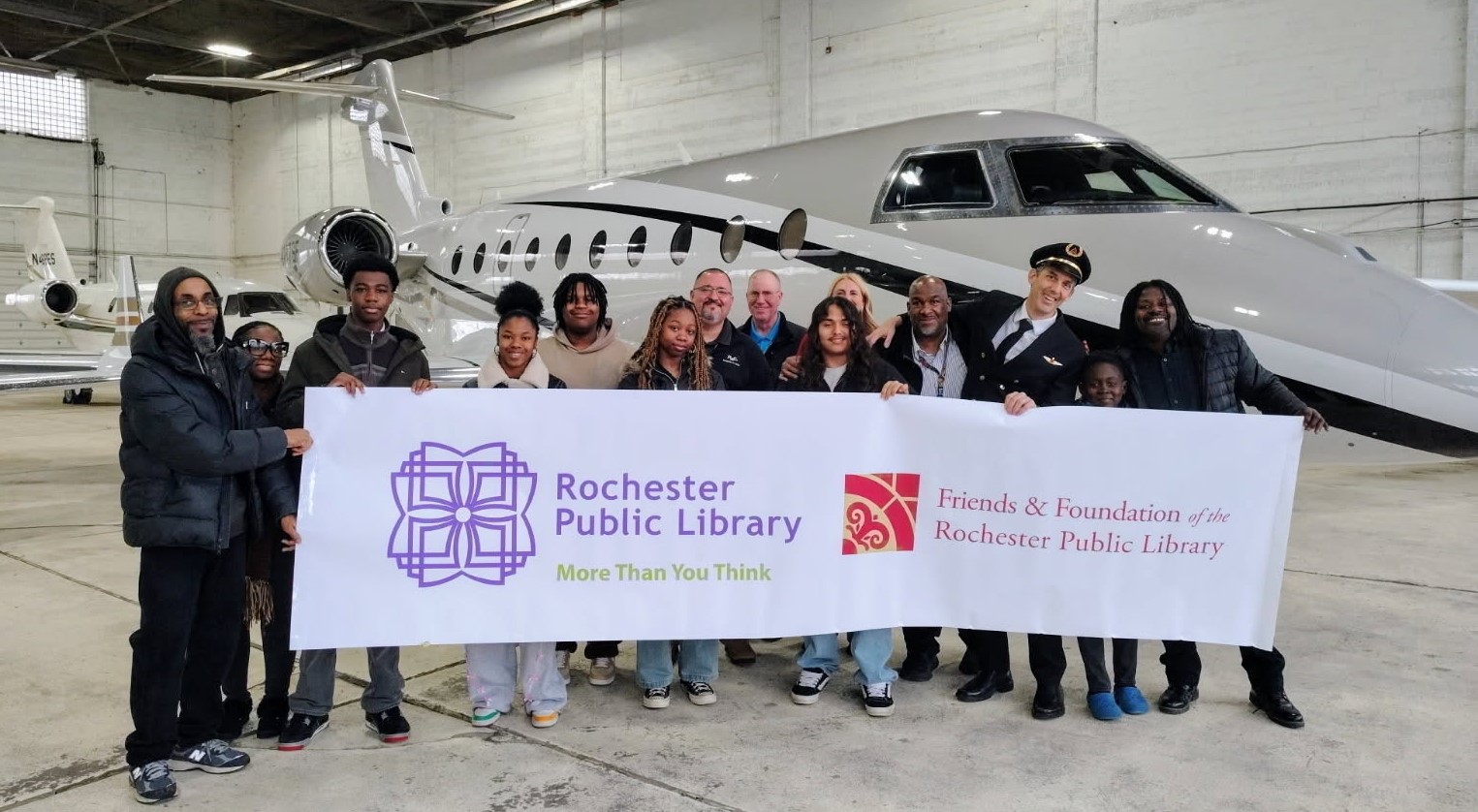 photo of Aviation Station you and staff with banner in front of plane